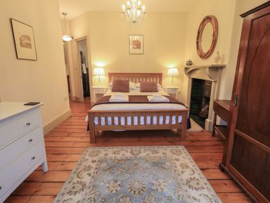 A bedroom with a wooden bed two bedside tables with lamps a chest of drawers a wooden wardrobe and a fireplace at Fairy Glen in Grasmere near Ambleside