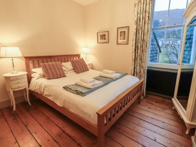 A bedroom with a wooden bed two bedside tables with lamps a window and a wardrobe at Fairy Glen in Grasmere near Ambleside