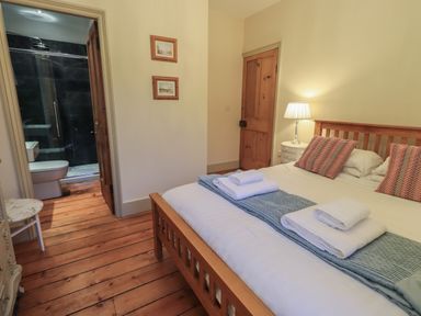 A bedroom with a wooden bed and folded towels next to an en suite bathroom at Fairy Glen in Grasmere near Ambleside