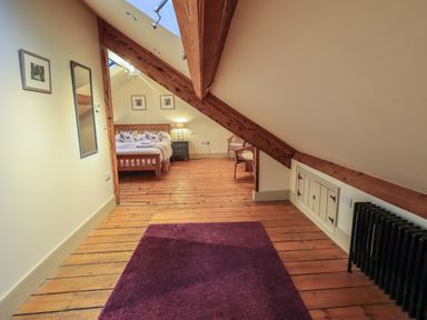 A bedroom with a wooden bed and nightstand under a sloped ceiling with exposed beams at Fairy Glen in Grasmere near Ambleside