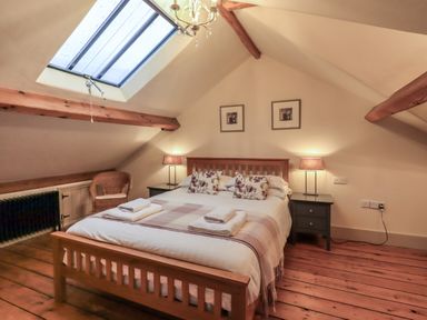 A bedroom with a wooden bed two bedside tables lamps a skylight and wooden floor at Fairy Glen in Grasmere near Ambleside