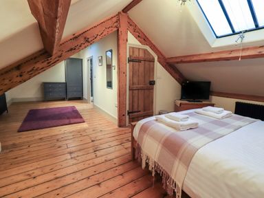 A bedroom with a wooden floor two gray dressers a purple rug a wooden door a skylight bed with folded towels and a television at Fairy Glen in Grasmere near Ambleside