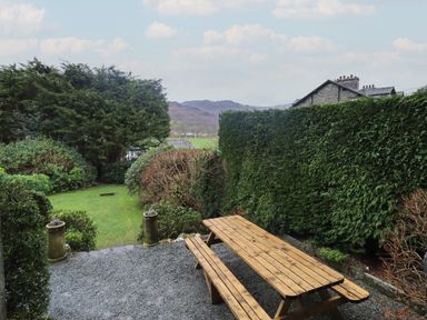 A wooden picnic table on a gravel area surrounded by trimmed hedges and garden with bushes at Fairy Glen in Grasmere near Ambleside