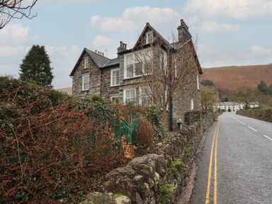 A stone house near a road with a stone wall and leafless trees at Fairy Glen in Grasmere near Ambleside