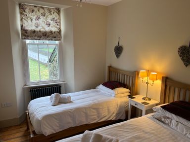 A bedroom with two single beds side by side a window with floral blinds and a bedside table with a lamp at Fairy Glen in Grasmere near Ambleside