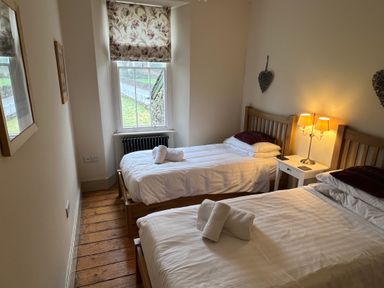 A bedroom with two single beds a window with floral blinds and a bedside table with a lamp at Fairy Glen in Grasmere near Ambleside