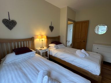 A bedroom with two single beds a nightstand with a lamp wooden door and dresser at Fairy Glen in Grasmere near Ambleside