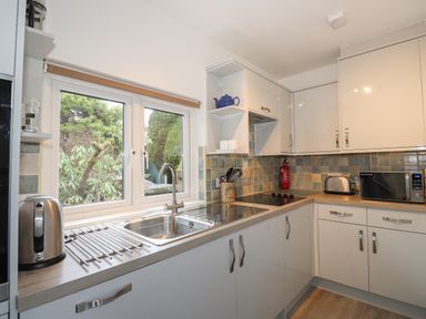 A kitchen with a sink under a window a kettle a toaster a microwave and cabinets at Larch Cottage in Hawkshead
