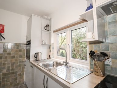 A kitchen with a sink under a window kettle utensils and tiled walls at Larch Cottage in Hawkshead