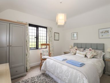 A bedroom with a double bed with pillows towels beside a window with curtains and a wooden chair at Larch Cottage in Hawkshead
