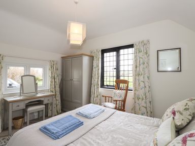 A bedroom with a bed, dressing table, wardrobe, wooden chair, and windows with floral curtains at Larch Cottage in Hawkshead