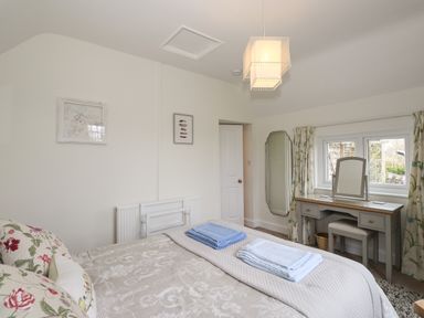 A bedroom with a bed with folded towels a dressing table with a mirror and curtains on the window at Larch Cottage in Hawkshead