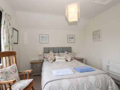 A bedroom with a bed pillows bedside tables lamps a wooden chair and framed pictures on the walls at Larch Cottage in Hawkshead