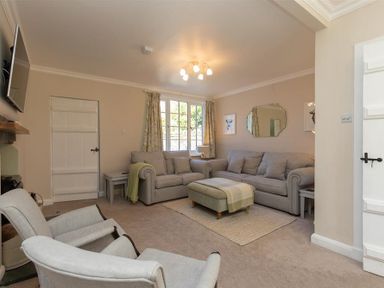 A living room with two sofas a cushioned ottoman two armchairs a wall-mounted tv and a window at Crozier Cottage in Grasmere