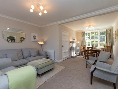 A living room with gray sofa and green ottoman adjacent to a dining area with wooden table and chairs at Crozier Cottage in Grasmere