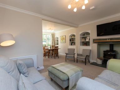 A living room with sofas armchairs a wood burner tv and a dining area with a table and chairs at Crozier Cottage in Grasmere