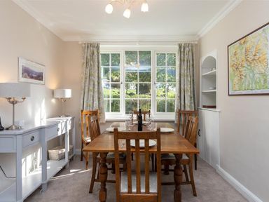 A dining room with a wooden table and chairs next to a window with floral curtains at Crozier Cottage in Grasmere