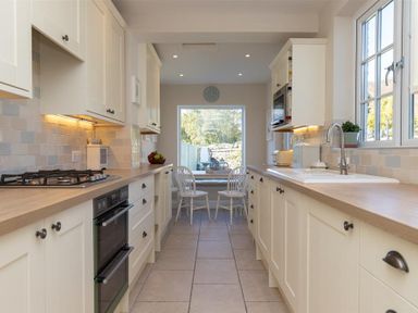 A kitchen with white cabinets a wooden countertop a stove and oven a sink and two chairs at a table by a window at Crozier Cottage in Grasmere