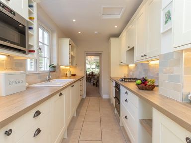 A galley kitchen with white cabinets and wooden countertops featuring a sink, microwave, stove, bread box, and a bowl of fruit at Crozier Cottage in Grasmere