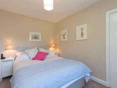 A bedroom with a double bed white bedding two bedside tables with lamps and animal artwork on walls at Crozier Cottage in Grasmere