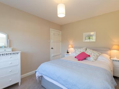 A bedroom with a bed with pillows and blankets two bedside tables with lamps a dresser with a mirror and a door at Crozier Cottage in Grasmere