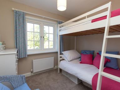 A bedroom with a white bunk bed with pink and blue pillows and a window with blue curtains at Crozier Cottage in Grasmere
