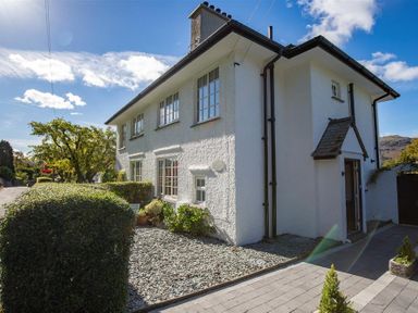 A white two-story house with multiple windows and a small porch over the entrance at Crozier Cottage in Grasmere