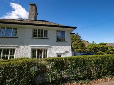Exterior of a white two-story house with multiple windows and a hedge in front at Crozier Cottage in Grasmere