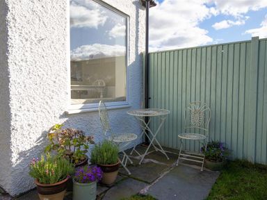 A small outdoor patio with two metal chairs and a round metal table beside potted plants at Crozier Cottage in Grasmere