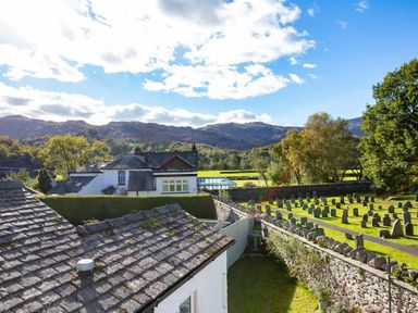 A view of rooftops trees and gravestones with hills in the background at Crozier Cottage in Grasmere