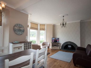 A living room with a dining table chairs a television fireplace and armchairs at Waterside Ambleside