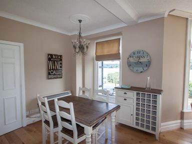 A dining room with a wooden table and white chairs a cabinet and a window at Waterside in Ambleside