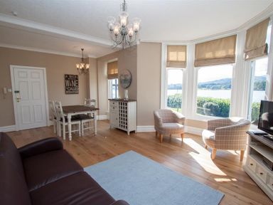 A living room with a brown sofa two armchairs a dining table with chairs wooden floor and large windows at Waterside Ambleside