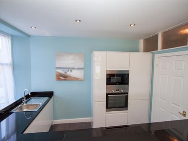 A kitchen with a black countertop a sink built in oven and microwave white cabinets and a painting on the wall at Waterside Ambleside