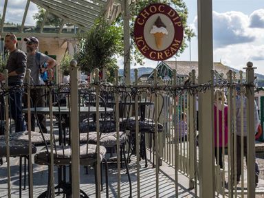 An outdoor seating area with tables and chairs under a glass roof near a choc dip ice cream sign