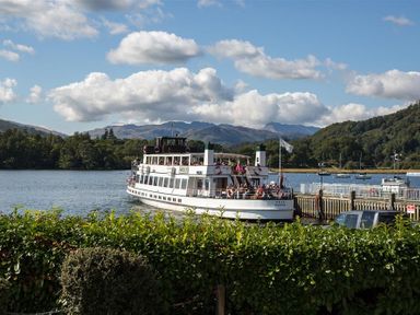 A boat on a lake near a dock with trees and hills in the background at Waterside in Ambleside