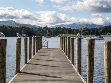 A wooden jetty with seagulls on posts overlooking a lake with boats and hills in the background at Waterside in Ambleside