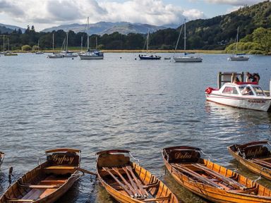 A lake with wooden rowboats and sailboats with mountains and trees in the background at Waterside in Ambleside