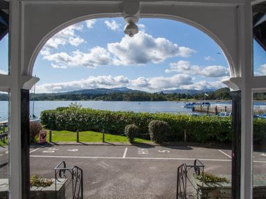 A view of a lake and hills through an arched porch with a parking area in front at Waterside in Ambleside