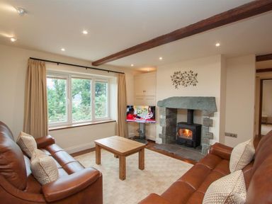 A living room with two leather sofas a wooden coffee table stone fireplace and a window at Dancing Beck Cottage in Millbeck