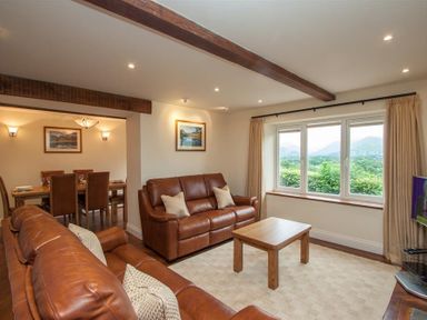 A living room with two leather sofas a wooden coffee table and a window showing a mountain view at Dancing Beck Cottage in Millbeck