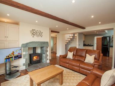 A living room with a wood burning stove and two brown leather sofas at Dancing Beck Cottage in Millbeck