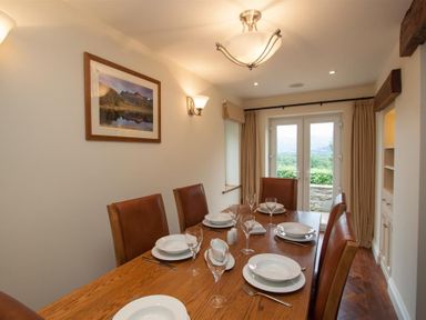 A dining room with a wooden table set with plates and glasses and leather chairs near a glass door at Dancing Beck Cottage in Millbeck