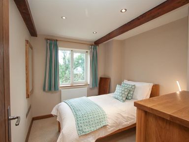 A small bedroom with a bed, wooden dresser, window with curtains, and exposed ceiling beams at Dancing Beck Cottage in Millbeck