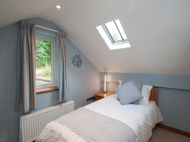 A bedroom with a single bed a skylight window a bedside table lamp and a window with curtains at Dancing Beck Cottage Millbeck