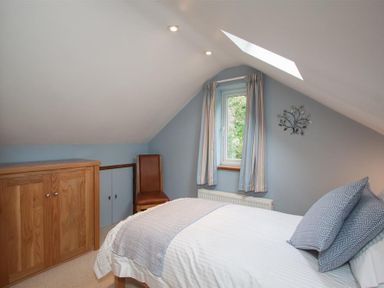 A bedroom with a bed a wooden chest of drawers a chair and a window with curtains at Dancing Beck Cottage in Millbeck