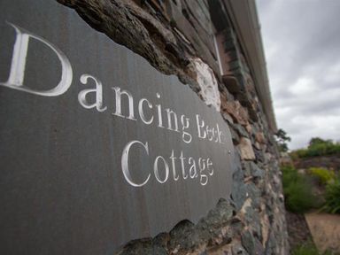 A stone wall with a plaque that reads Dancing Beck Cottage in Millbeck