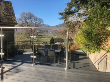 An outdoor patio with glass railing chairs and a table with countryside view at Dancing Beck Cottage in Millbeck