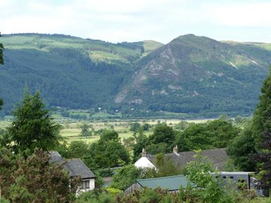 A rural landscape with houses trees and a mountain in the background at Dancing Beck Cottage in Millbeck