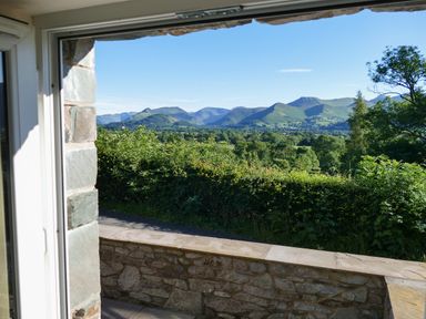 A view of green hills and trees from a stone walled patio at Dancing Beck Cottage in Millbeck